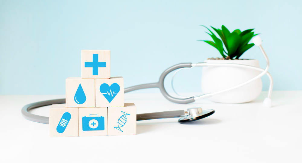 Pyramide de cubes en bois avec des symboles médicaux posée à côté d'un stéthoscope pour illustrer les bases des soins santé