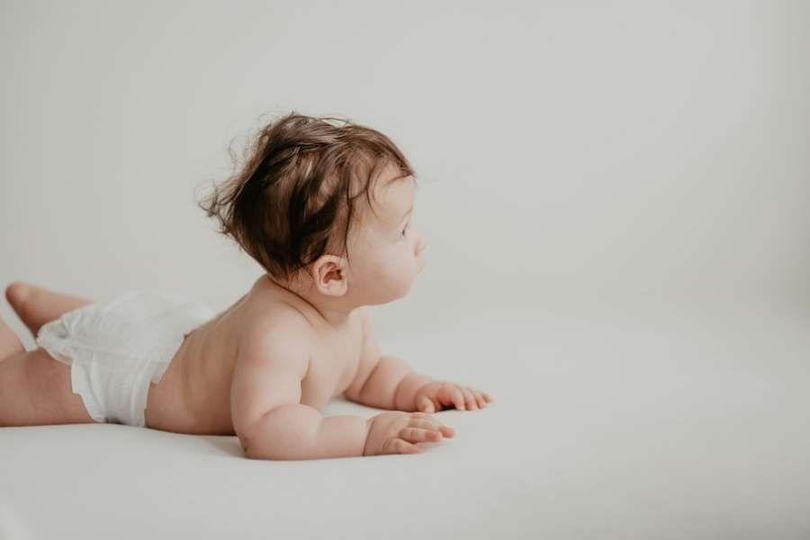Un bébé est allongé sur le ventre sur un fond neutre, mettant en valeur la douceur de la peau fragile de bébé.