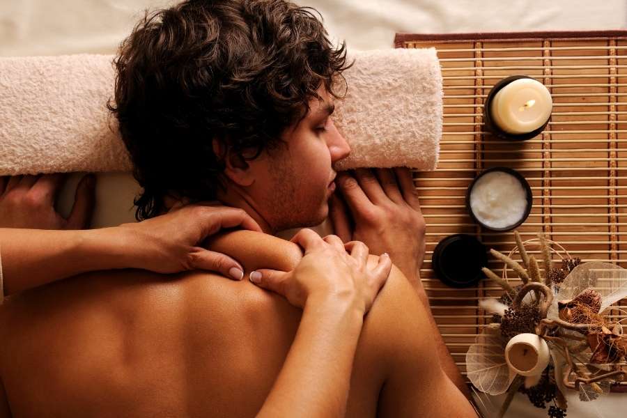 Gros plan d'un homme détendu, les yeux fermés, allongé sur le ventre et recevant un massage relaxant du dos par les mains d'un praticien sur une table de massage en bambou.