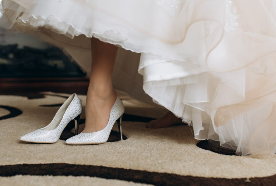 Mariée enfilant ses escarpins blancs, des chaussures confortables mariee pour danser toute la nuit sous sa robe en tulle.